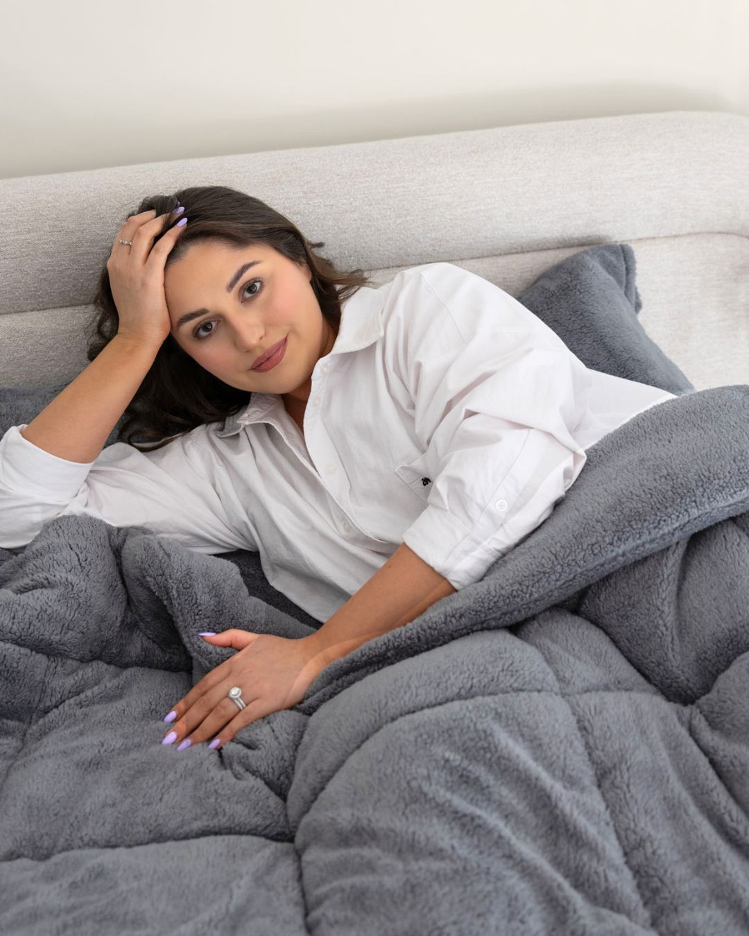 Woman lying on a bed under a gray weighted blanket