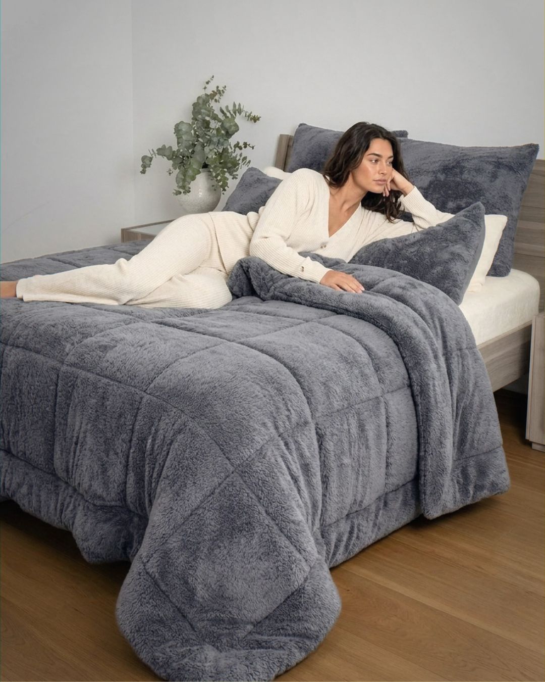 Woman lying on a bed with a gray comforter in a cozy bedroom setting.