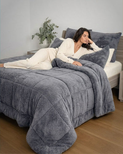 Woman lying on a bed with a gray comforter in a cozy bedroom setting.
