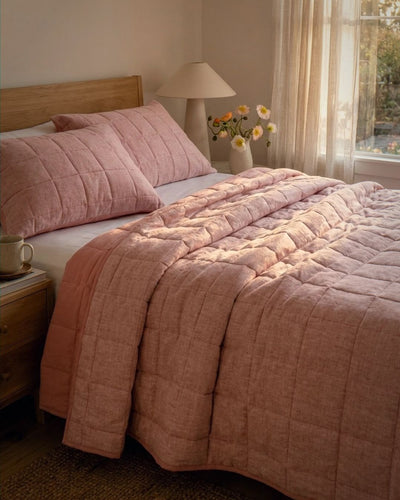 Bedroom with pink quilt and pillows, nightstand with mug and lamp.