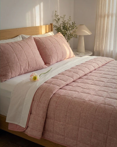 Bed with pink bedding and pillows in a softly lit bedroom.