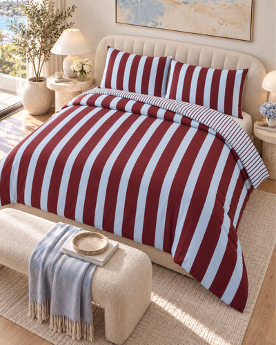 A bed dressed in a red and white striped duvet cover and matching pillowcases, styled in a bright bedroom with a cream upholstered headboard, bedside tables, lamps, and a bench at the foot of the bed.