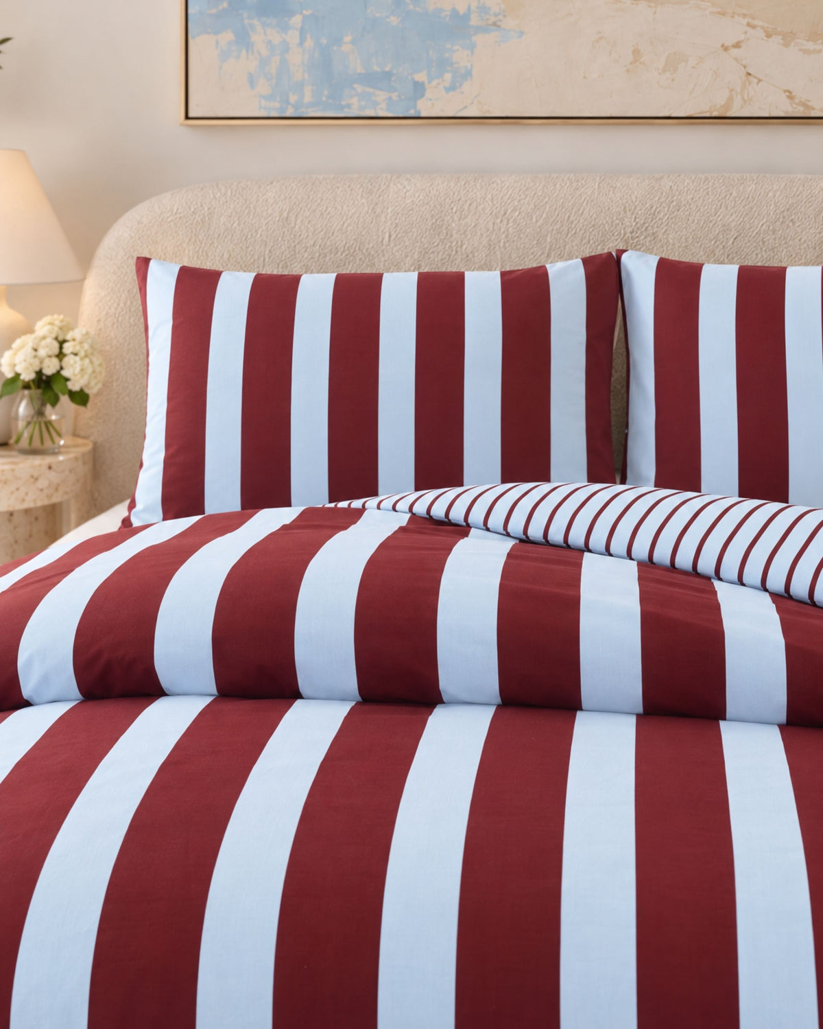 Red and white vertically striped bedding set including a duvet cover and two matching pillowcases, styled on a bed with a beige upholstered headboard in a bedroom setting.