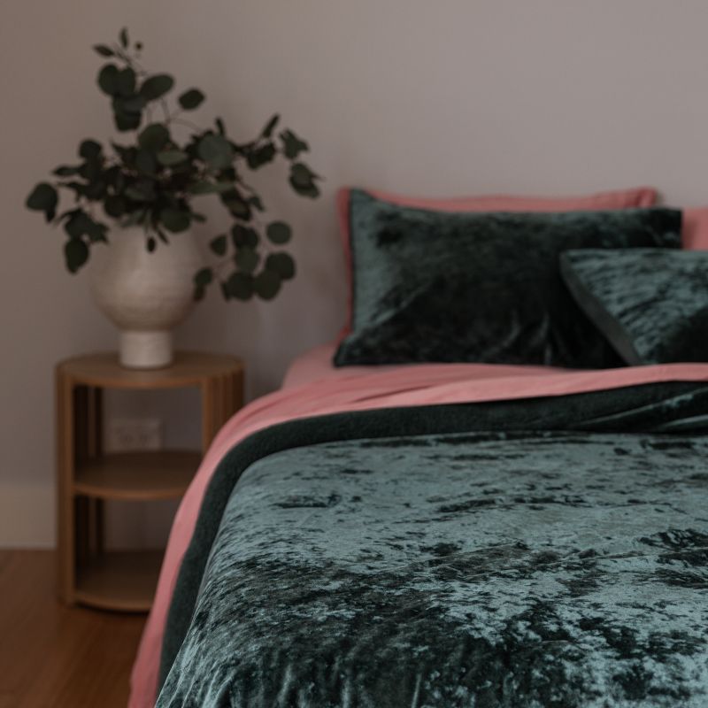 Bed with pink and green bedding, nightstand with plant, and wooden floor.
