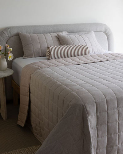 Neatly made bed with gray bedding and pillows in a bedroom setting.