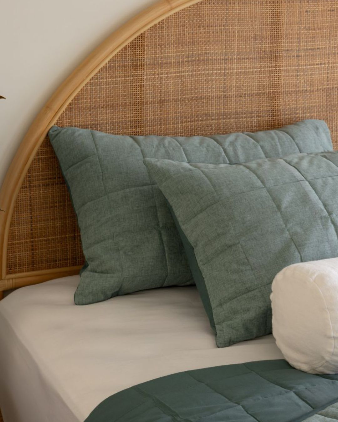 Bed with green pillows and a wicker headboard