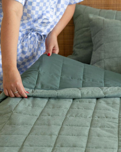 Person folding a green quilt on a couch