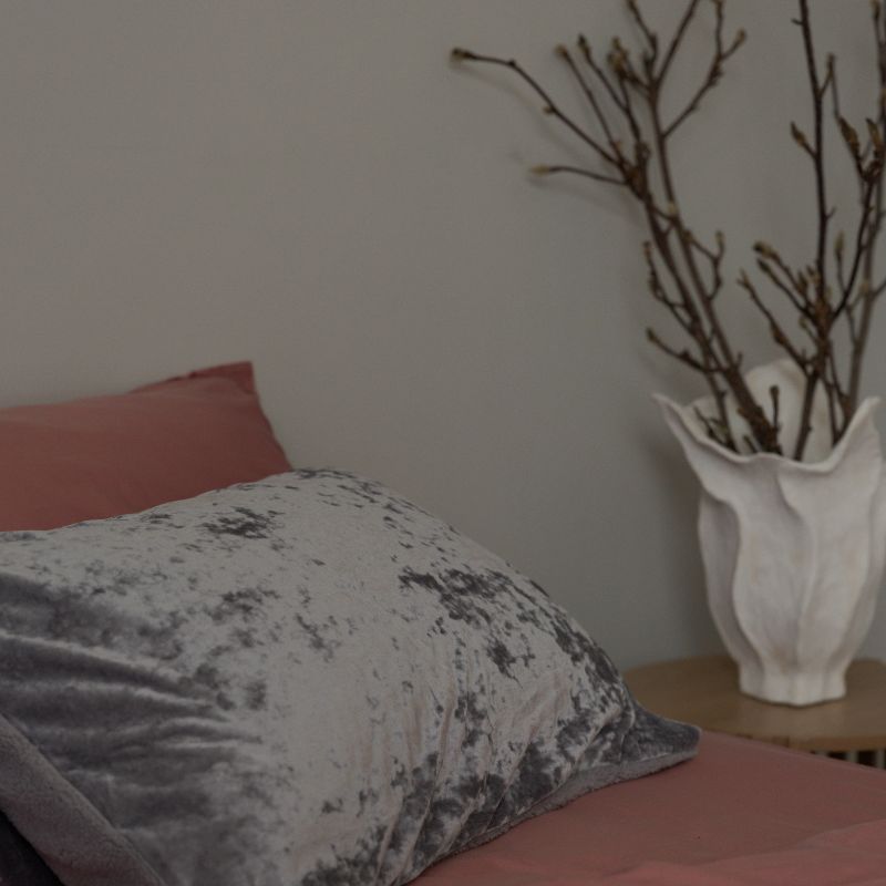 Gray pillow on a bed with a vase of branches in the background