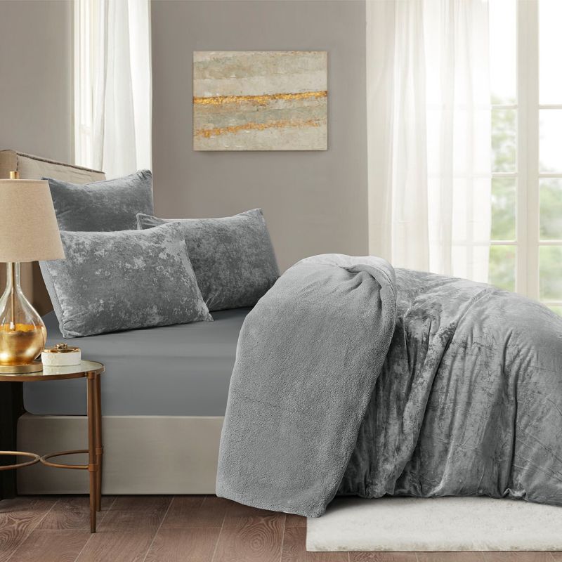 Gray bedding set on a bed in a bedroom with a lamp and painting on the wall.