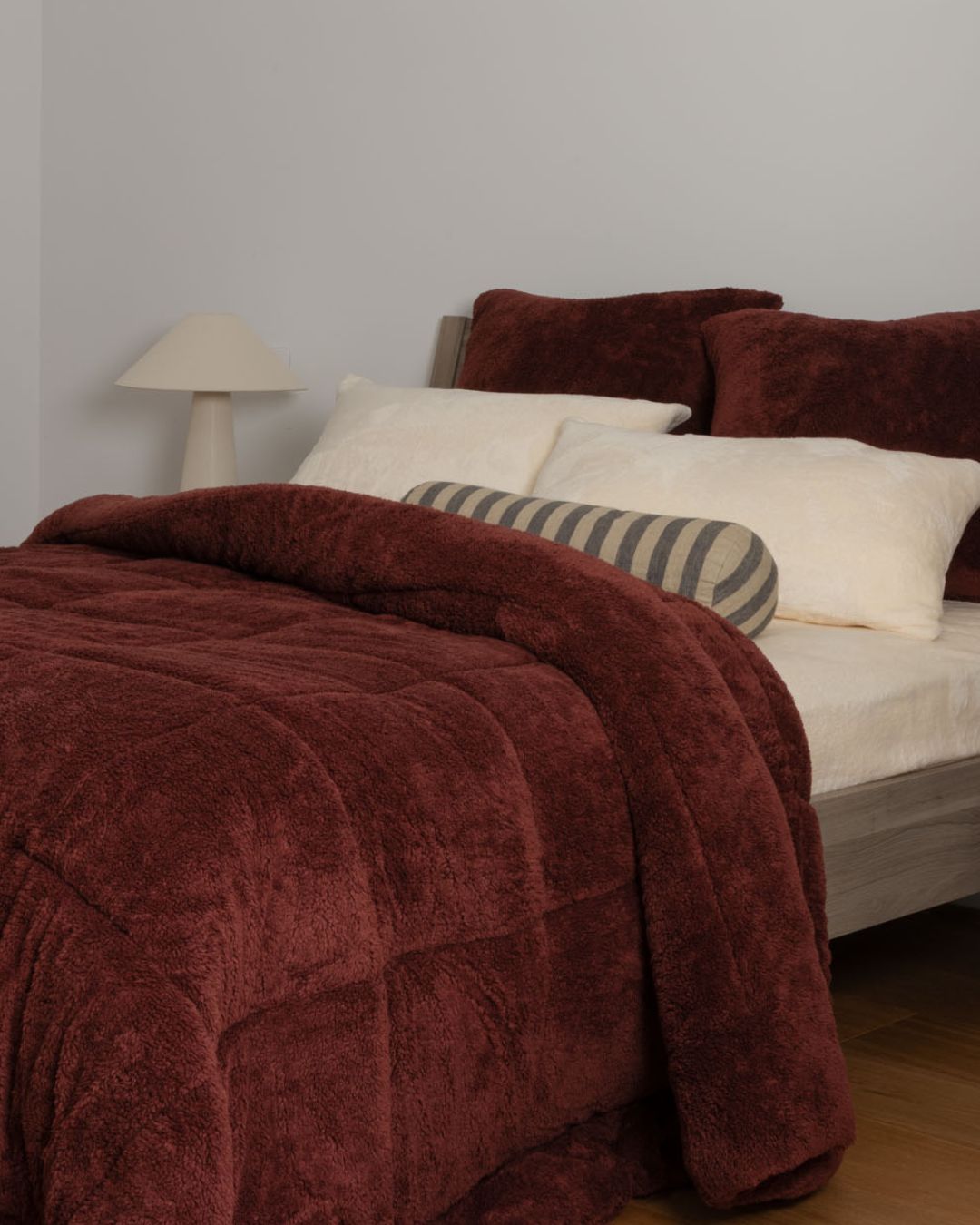 Hot chocolate comforter on a bed with pillows against a plain wall.