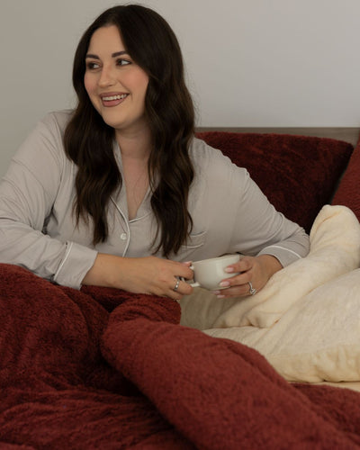 Woman sitting on a couch holding a mug, wrapped in a blanket