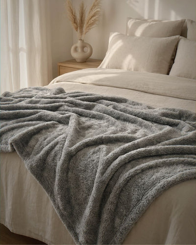 Gray blanket draped over a bed with neutral bedding and decor.