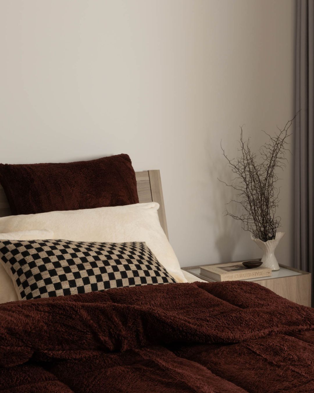Bed with brown blanket and pillows, nightstand with decorative items in the background