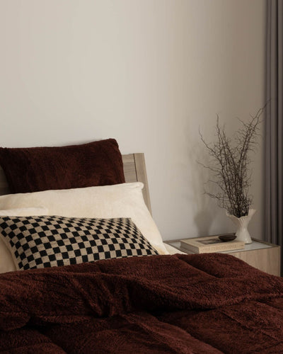 Bed with brown blanket and pillows, nightstand with decorative items in the background