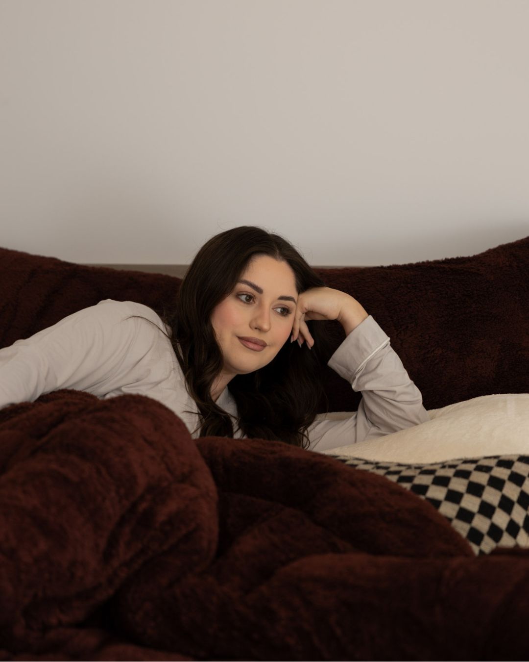 Woman lying on a brown couch with a blanket, looking relaxed.