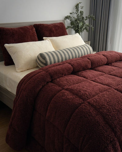 Bed with burgundy comforter and pillows in a bedroom setting
