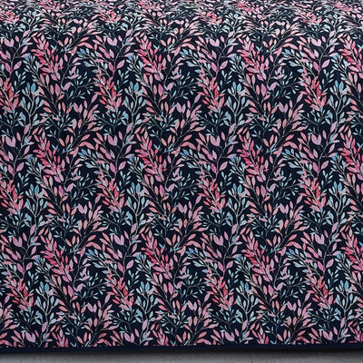 A neatly made bed with a dark floral comforter and matching pillows, the Morgan and Reid Sophia Coverlet Set in lightweight breathable fabric at the foot, a wooden headboard, geometric wall art, and a vase of flowers on the bedside table.