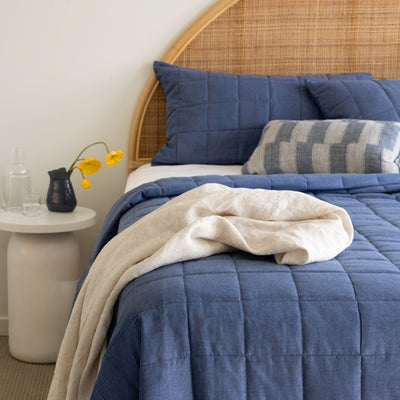 Bed with blue bedding and pillows, next to a side table with a vase and flowers.