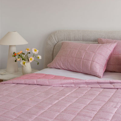 Bed with pink checkered bedding and pillows, nightstand with lamp and flowers.