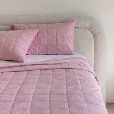 Pink quilted bedding set on a bed with a neutral headboard.