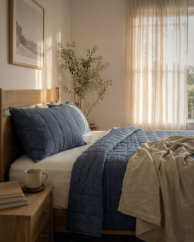 Bedroom with a bed featuring blue bedding and beige towel, wooden nightstand, and plant.