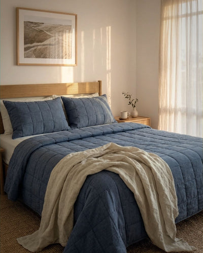Bedroom with a bed covered in blue bedding and a beige throw blanket, with a wooden headboard and framed picture on the wall.