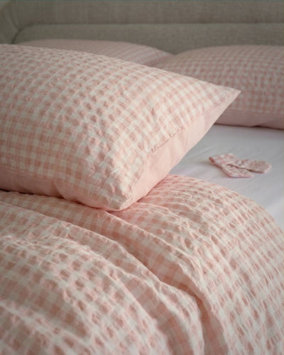 Pink checkered bedding set on a bed with pillows.