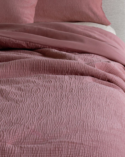 Close-up of textured pink bedding with a pillow in the background