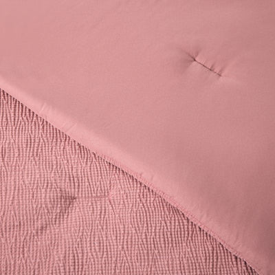 A modern bedroom features the Morgan and Reid Rose Stretch Woven Comforter Set on a neatly made bed with matching pillows, warm neutral walls, a woven pendant light, a wooden side table with a glass vase of white stems, and a ceramic lamp on a timber bedside table.