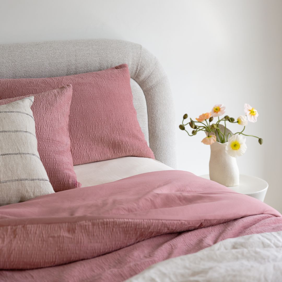 Pink textured bedding set on a bed with a vase of flowers on a nightstand.