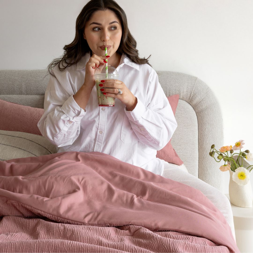 Woman sitting on a couch with pink blanket, drinking from a straw