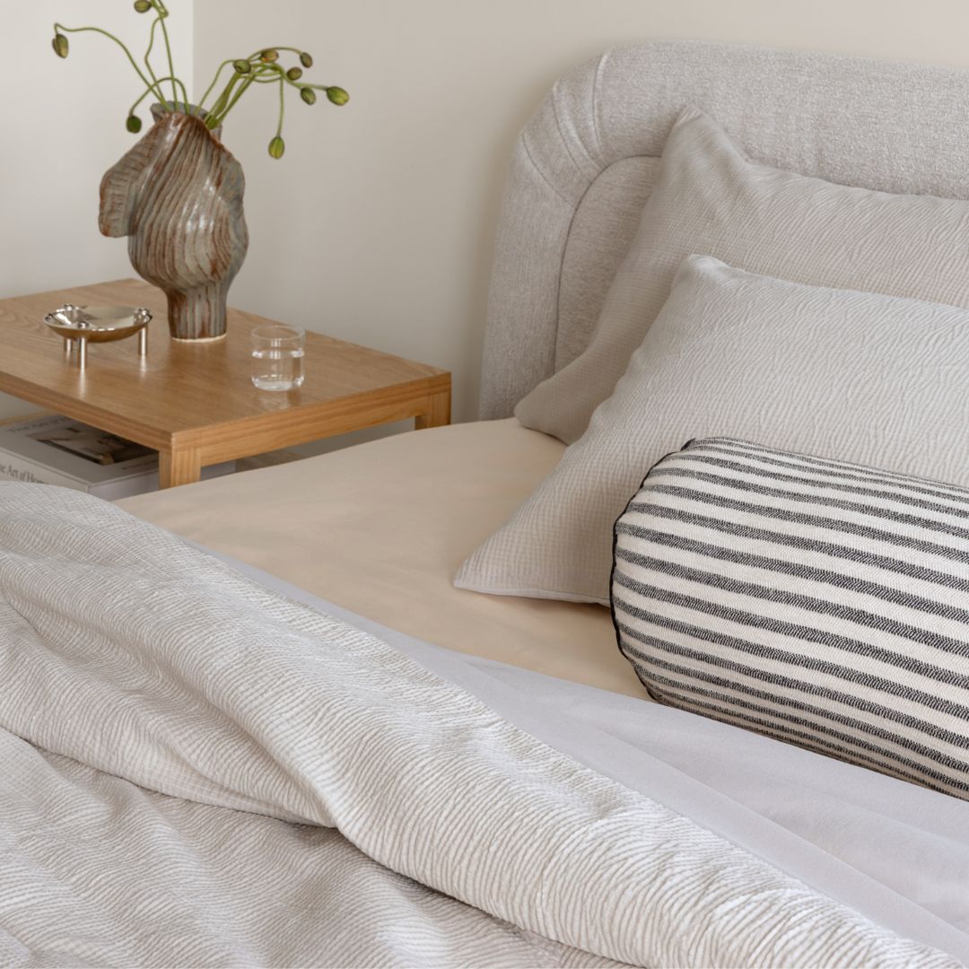 Neatly made bed with striped pillow and wooden side table with decorative items.