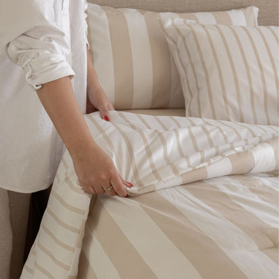 Person making a bed with beige and white striped bedding