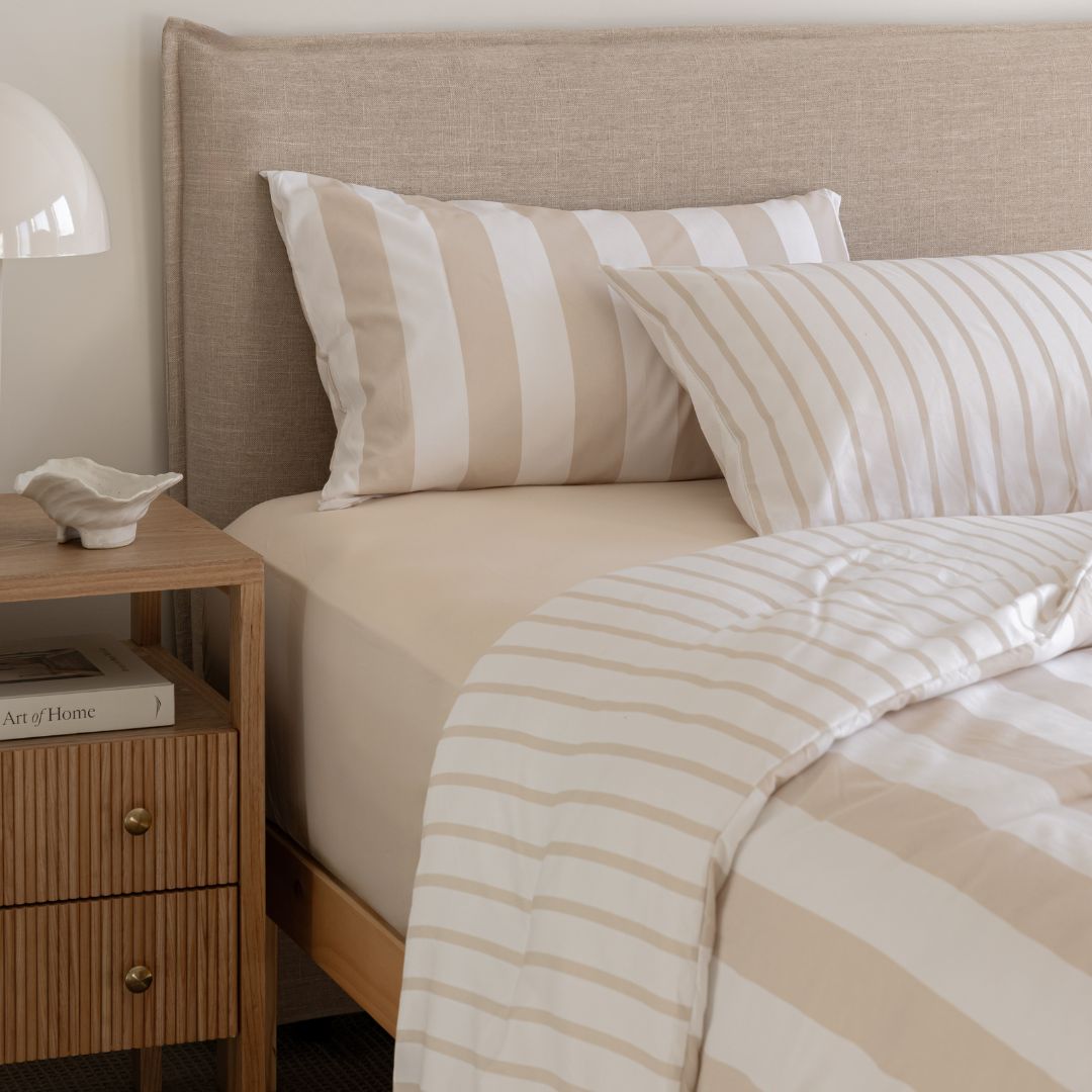 Beige and white striped bedding on a bed with a wooden nightstand.