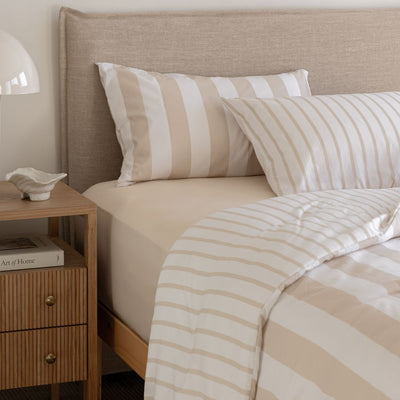 Beige and white striped bedding on a bed with a wooden nightstand.