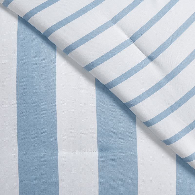 A fresh coastal bedroom features the Morgan and Reid Sea Breeze Stripe Comforter Set on a neatly styled bed with striped pillows, rattan bedhead, textured rug, natural pendant lighting, and a leafy plant beside the bed.