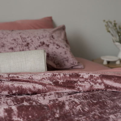 Pink textured blanket and pillows on a bed with a blurred background