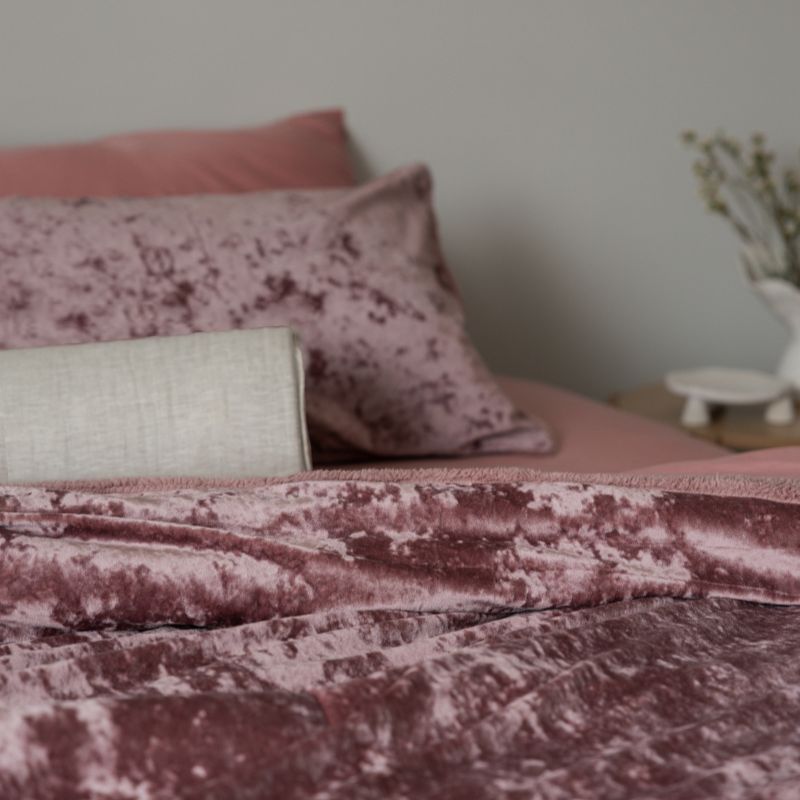 Pink textured blanket and pillows on a bed with a blurred background