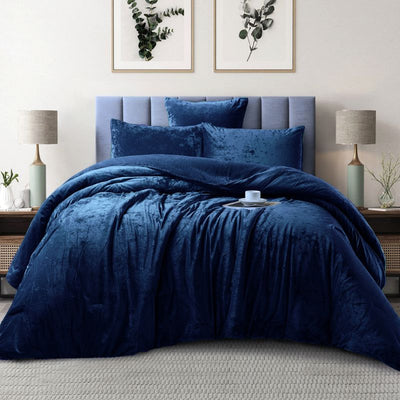 Blue velvet comforter set on a bed in a bedroom with lamps and wall art.