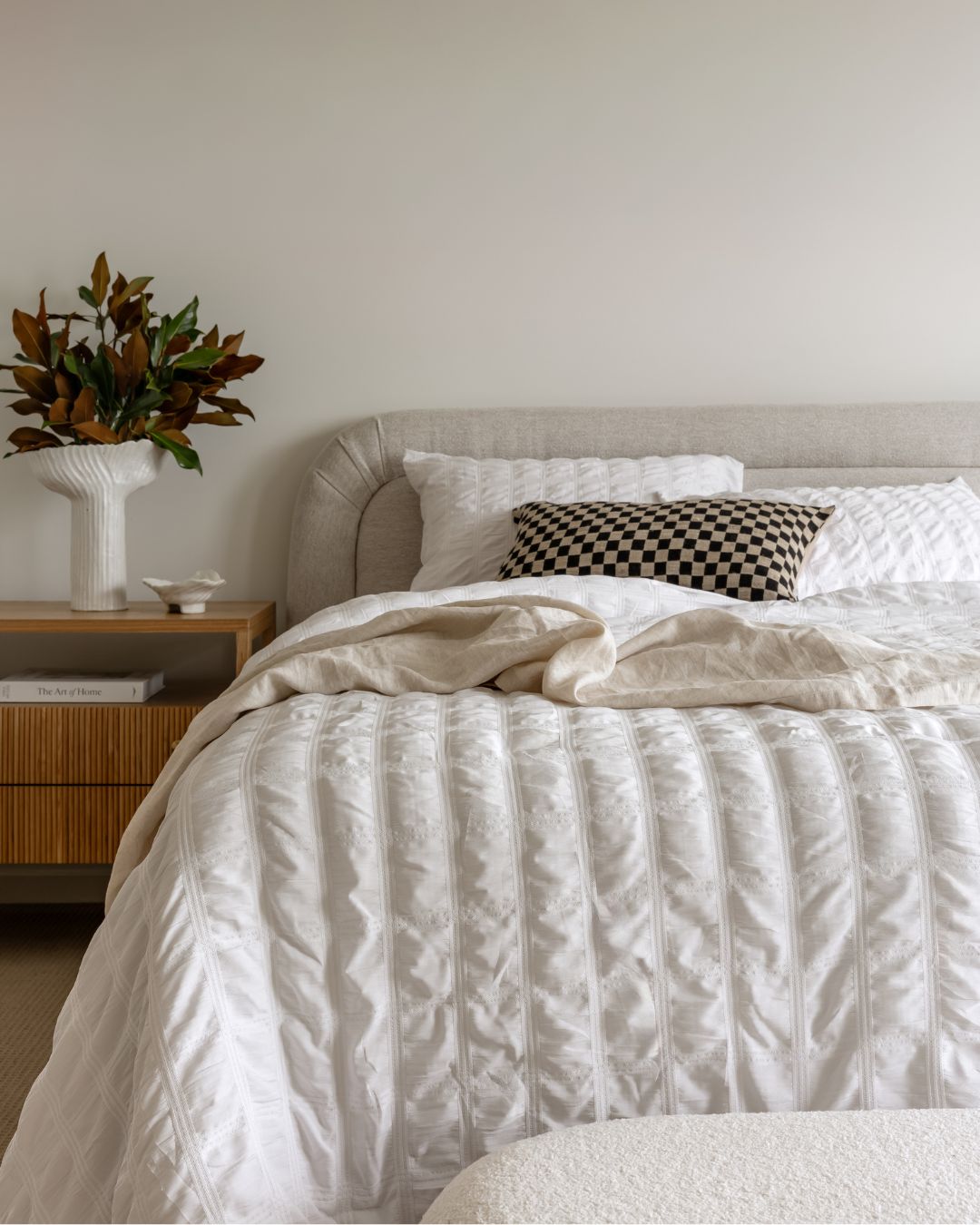 Neatly made bed with white bedding in a bedroom setting.