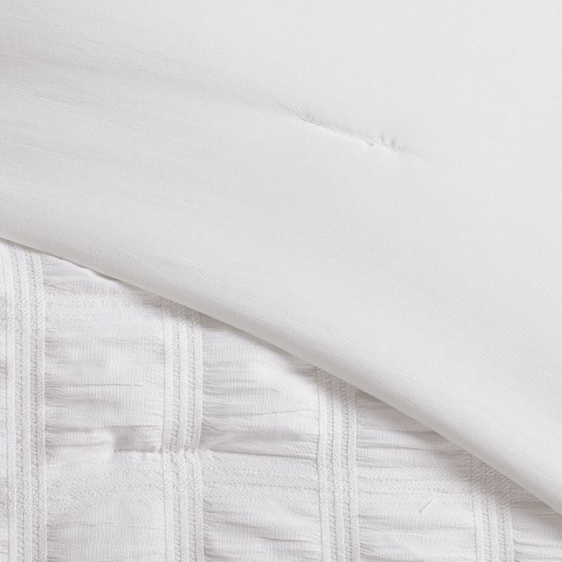 A clean modern bedroom highlights the Morgan and Reid Whispers of White Comforter Set with matching pillowcases, rattan bedhead, neutral-toned walls, woven pendant lamp, indoor greenery, and a simple wooden side table.