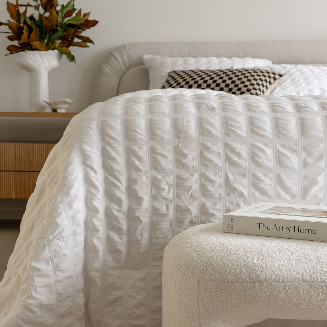 Neatly made bed with white bedding and a book titled 'The Art of Home' on a nightstand.