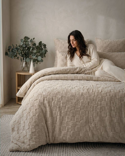 Lifestyle shot of Sand Checkered Snuggle Fleece Comforter Set on bed with woman in cozy cream loungewear
