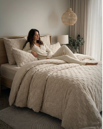Woman relaxing on Sand Checkered Snuggle Fleece Comforter Set in cozy neutral bedroom lifestyle shot