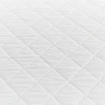 Close-up of the Sienna Living Premium Cotton Mattress Protector featuring a quilted cotton japara cover and diamond stitch pattern, fitted securely over a mattress with a grey upholstered base. Knit stretch skirt ensures a snug fit around corners.
