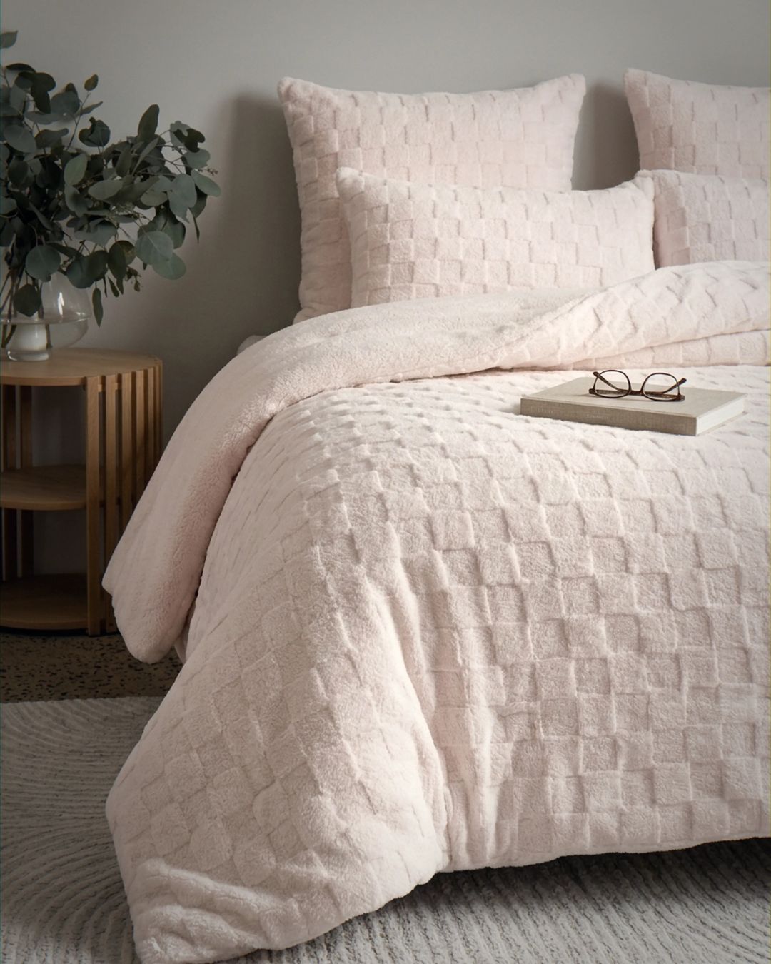 Soft pink checkered snuggle fleece comforter set styled on bed with matching pillows and eucalyptus decor