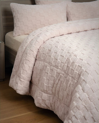 Soft pink checkered snuggle fleece comforter set styled on bed, showing plush quilted texture detail with matching pillowcases.